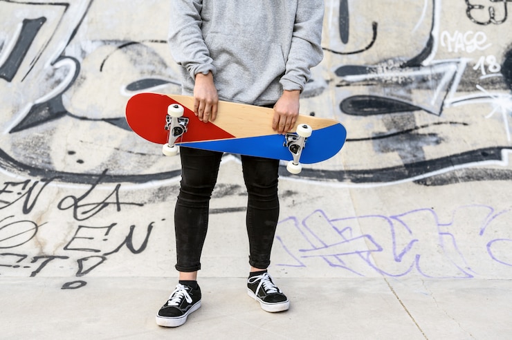 Foto close up of unrecognizable young man holding skateboard in the park.