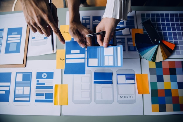 Close up ux developer and ui designer brainstorming about mobile app interface wireframe design on table with customer breif and color code at modern officeCreative digital development agency