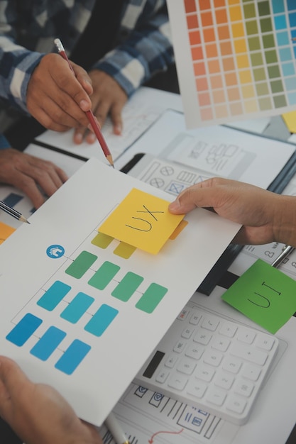 Close up ux developer and ui designer brainstorming about mobile app interface wireframe design on table with customer breif and color code at modern officeCreative digital development agency