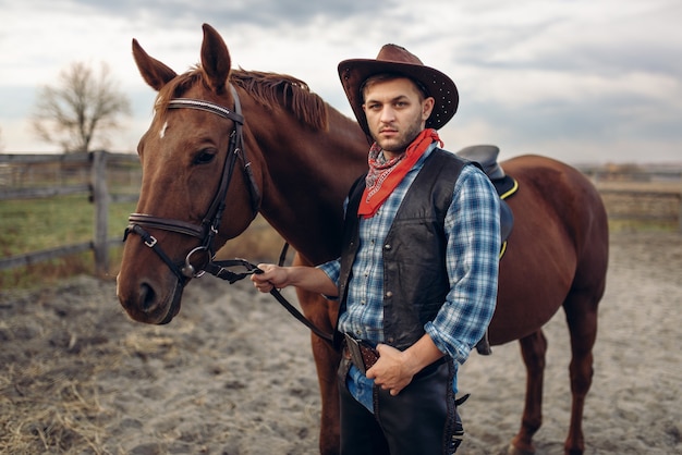 Cowboy in jeans and leather jacket poses with horse on texas farm