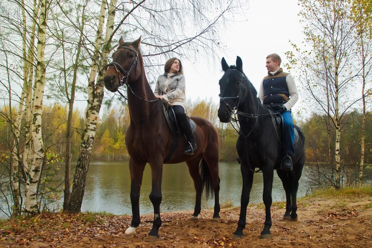 Foto cute young couple on horsebacks in the autumn forest by lake. riders in autumn park in inclement cloudy weather with light rain