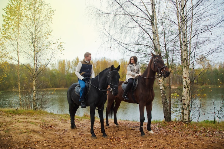 Foto cute young couple on horsebacks in the autumn forest by lake