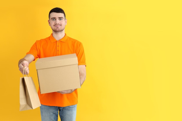 delivery man holds box and paper bag on yellow background
