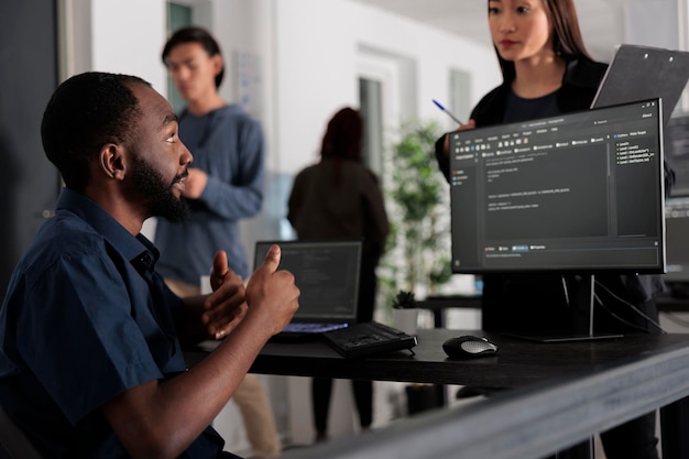 Diverse group of web developers analyzing html code and comparing data script in big data office room. Cloud programers working on system interface algorithm in development company.