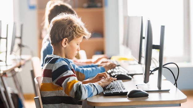 elementary school computer science classroom cute little boy uses personal computer learning programming language for software coding schoolchildren getting modern education side view portrait