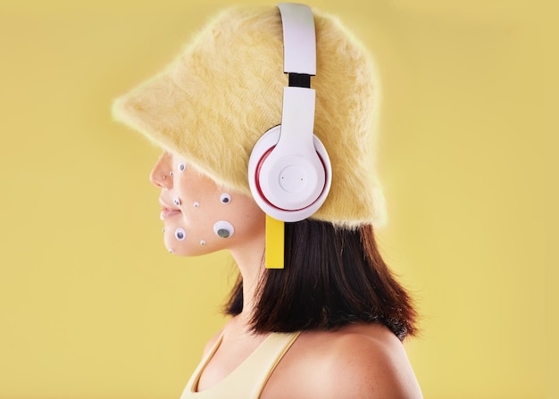 Eye stickers music headphones and woman in studio isolated on a yellow background mockup Funny technology and face profile of female listening enjoying and streaming radio podcast and audio