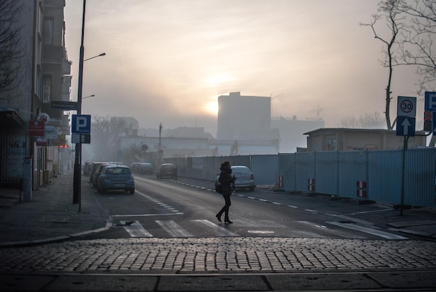 full length of woman crossing city street against sky during foggy weather