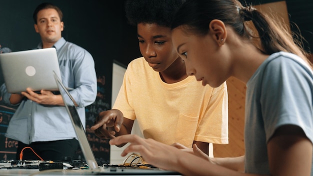 Girl programing or coding system while african boy fixing model Edification