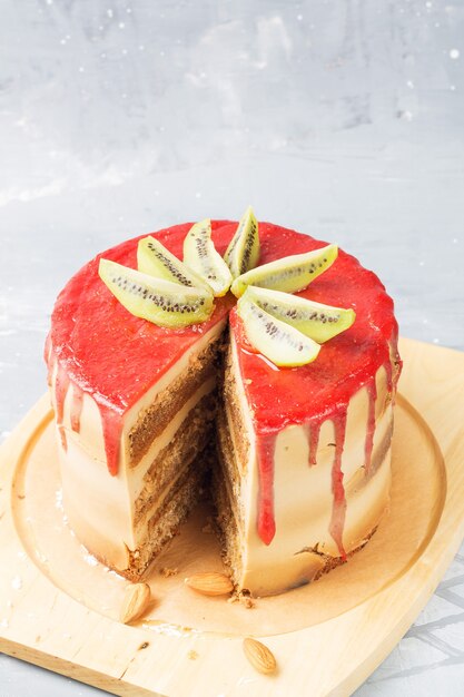 Glutenfri kake med jordbærfrosting, kokosflak og mandler på et stativ, dekorert med kiwiskiver. Frontskive av kaken. Kopi plass. Vertikal posisjon