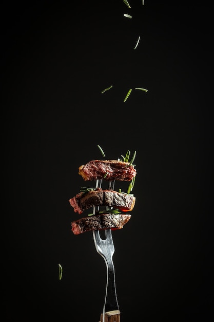 Grilled beef steak with spices on a black background Beef steak on a fork sprinkled with rosemary and sea salt