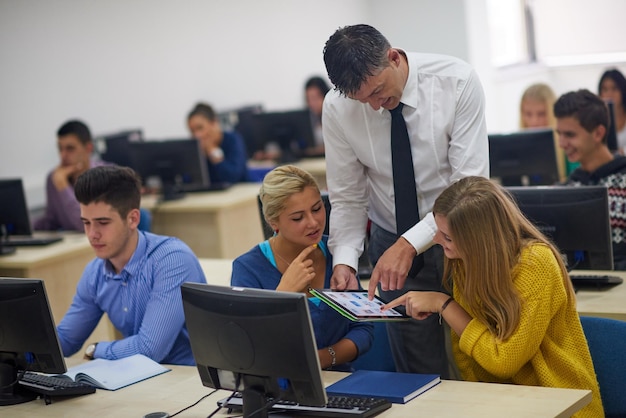 group of students with teacher in computer lab classrom learrning lessons get help and support