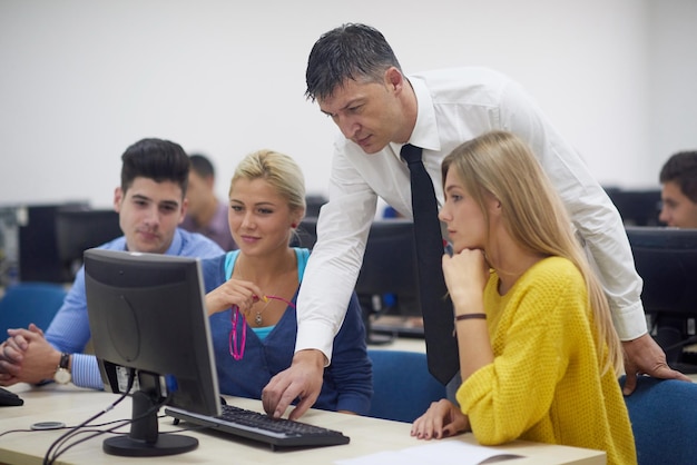 group of students with teacher in computer lab classrom learrning lessons get help and support