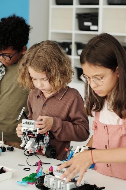 Group of youthful intercultural schoolchildren creating new toy robots
