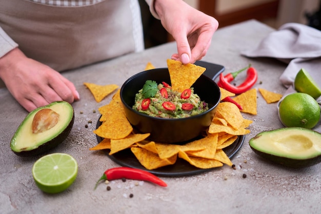 Guacamole dip with tortilla chips or nachos on black serving board
