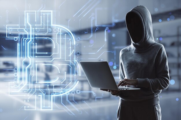 hacker holding laptop with creative glowing bitcoin circuit hologram on blurry office interior background cryptocurrency blockchain and finance concept double exposure