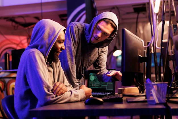 Hackers smiling while cracking encrypted information successfully on computer and working together in hideout place. Two criminals coding illegal malicious software for server hacking