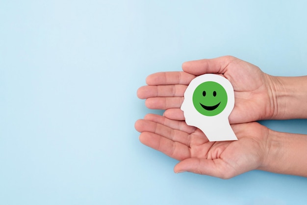 Hands holding paper cutout of head with smiling green emoji on blue backgroundcustomer satisfaction