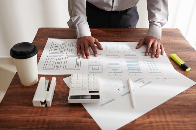 Hands of project manager leaning on table with printed mockups of mobile interface