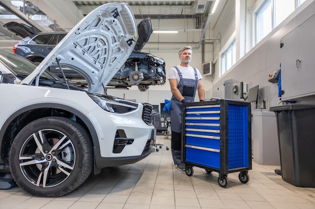 Handyman in auto workshop with equipment for labor work on vehicle repair and diagnostics
