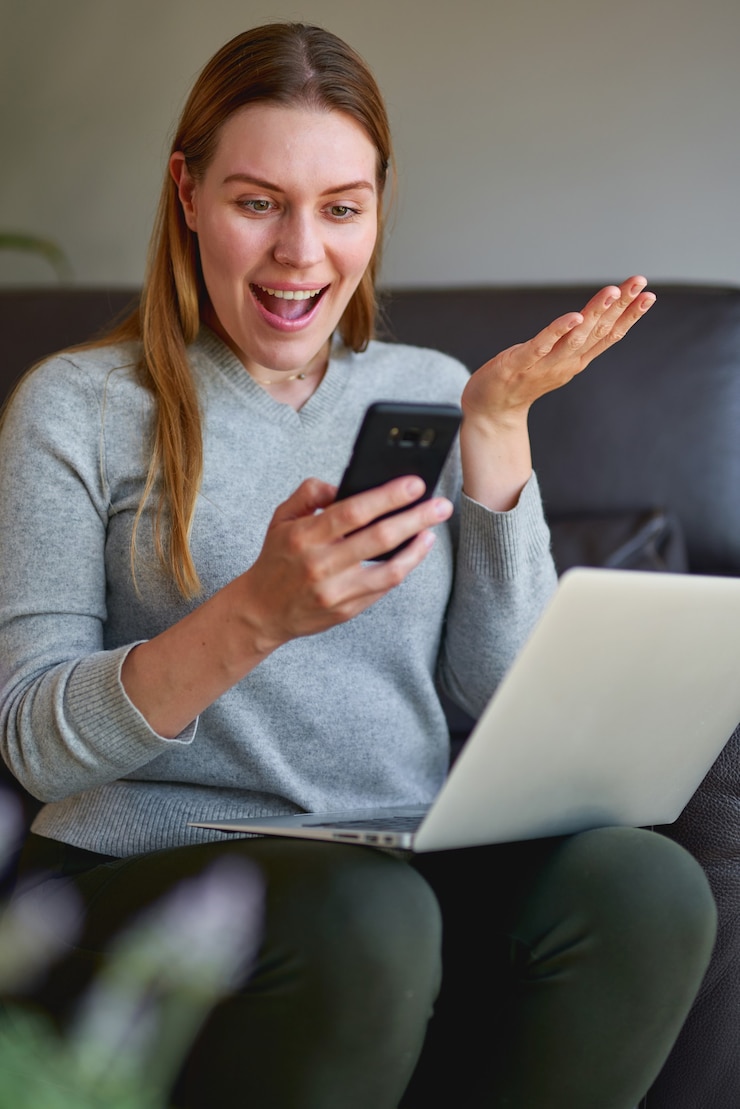 Foto happy woman sitting on sofa with laptop and talking on phone at home. college student studying on laptop and using phone.
