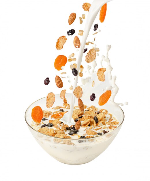 Heller melk og fallende musli over en gjennomsiktig bolle. Isolert på hvitt. Sunn frokost
