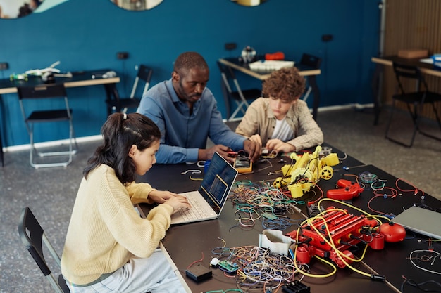 High angle portrait of young girl using laptop in engineering class and programming robots copy spac