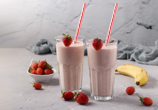 Hjemmelaget smoothie med jordbær og banan i to glass med sugerør på lysegrå bakgrunn