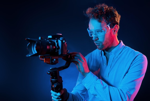 Holds camera Neon lighting Young european man is in the dark studio