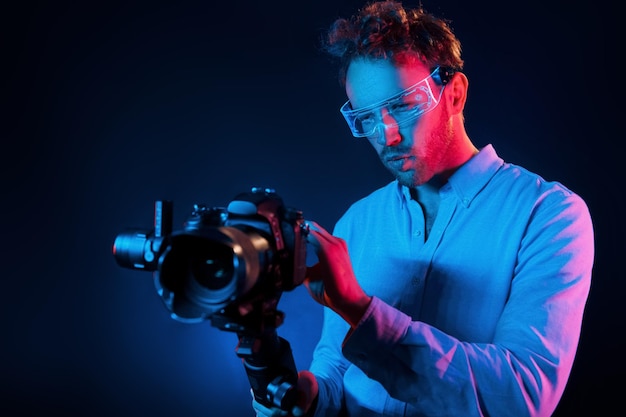 Holds camera Neon lighting Young european man is in the dark studio