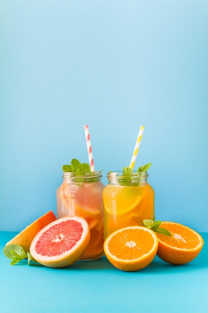 Jars with orange and grapefruit lemonade decorated ice and mint on blue paper background