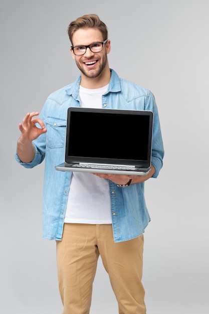 Konsentrert, ung mann med skjegg som bruker briller og er kledd i jeansskjorte, holder en laptop