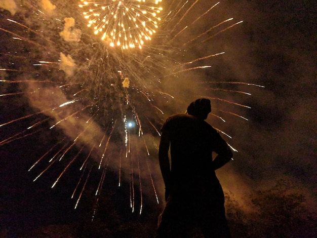 low angle view of man looking at firework display against sky