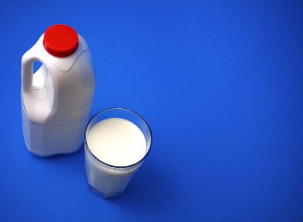 Lufttett en gallon melkekanne med rød kork og fullt glass melk på blå vegg