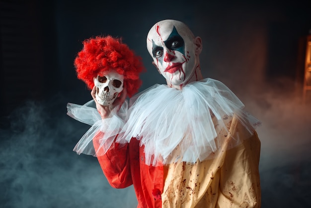 mad bloody clown holds human skull in red wig