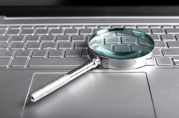 magnifying glass on laptop keyboard internet surfing concept online databases study audit conducting using computer