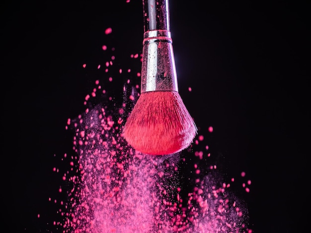 Makeup brush with pink powder splashes explosion on black background Beauty concept