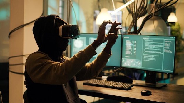 Male cyber criminal hacking network system with vr headset, using virtual reality to steal passwords and info illegally. Young adult using hacktivism skills to break into security server.
