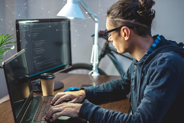 male programmer is writing program code on a laptop at home
