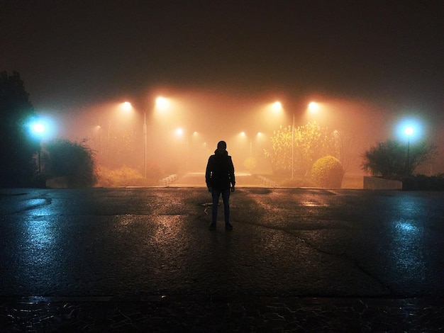 Man standing on street against illuminated street light at night
