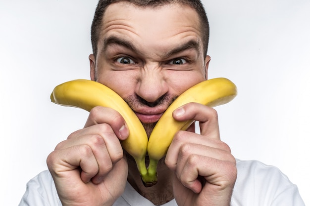 Mann i hvit skjorte holder to bananer tett inntil ansiktet