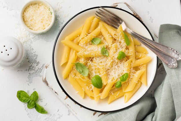 Penne rigate pasta med parmesanost og basilikumblader i keramisk fat på lett gammelt betongbord.