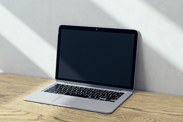 Perspective view on blank dark modern laptop screen with place for web site or design on wooden surface and sunlit wall background outdoor advertising and marketing concept 3D rendering mock up