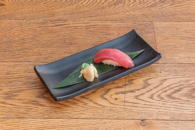 piece of high quality red tuna nigiri served on a banana leaf on a black plate with wasabi and ginseng