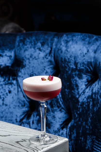 Pink Clover Club Cocktail in Coupe Glass with Layer of Foam and flower Garnish isolated on dark Background