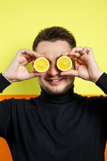 Portrait of a man in black raglan with cut lemon instead of eyes. A guy with lemons near his face. A smile on his face