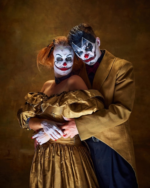portrait of two sinister clowns couple dressed vintage attire hugs together against background