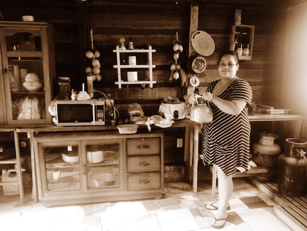 Portrait of woman holding teapot while standing in kitchen at home