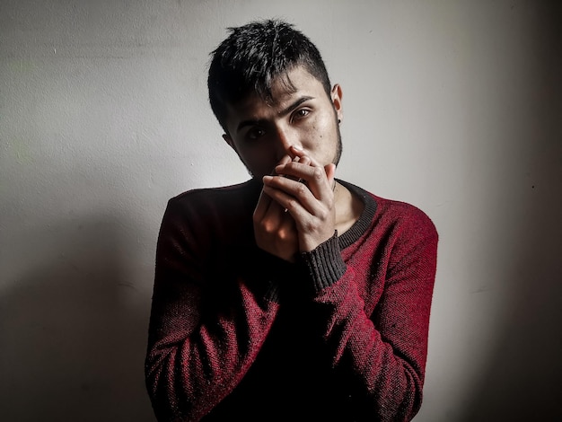 Portrait of young man with hands covering mouth against wall