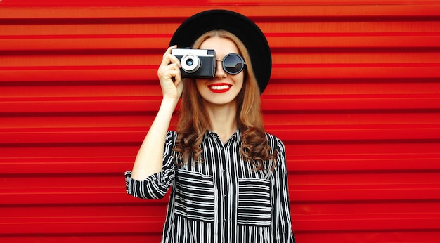 portrait young woman photographer with vintage film camera over red wall background