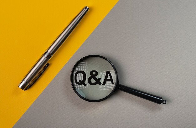 Q or qa concept through magnifying glass on yellow and gray colored table.
